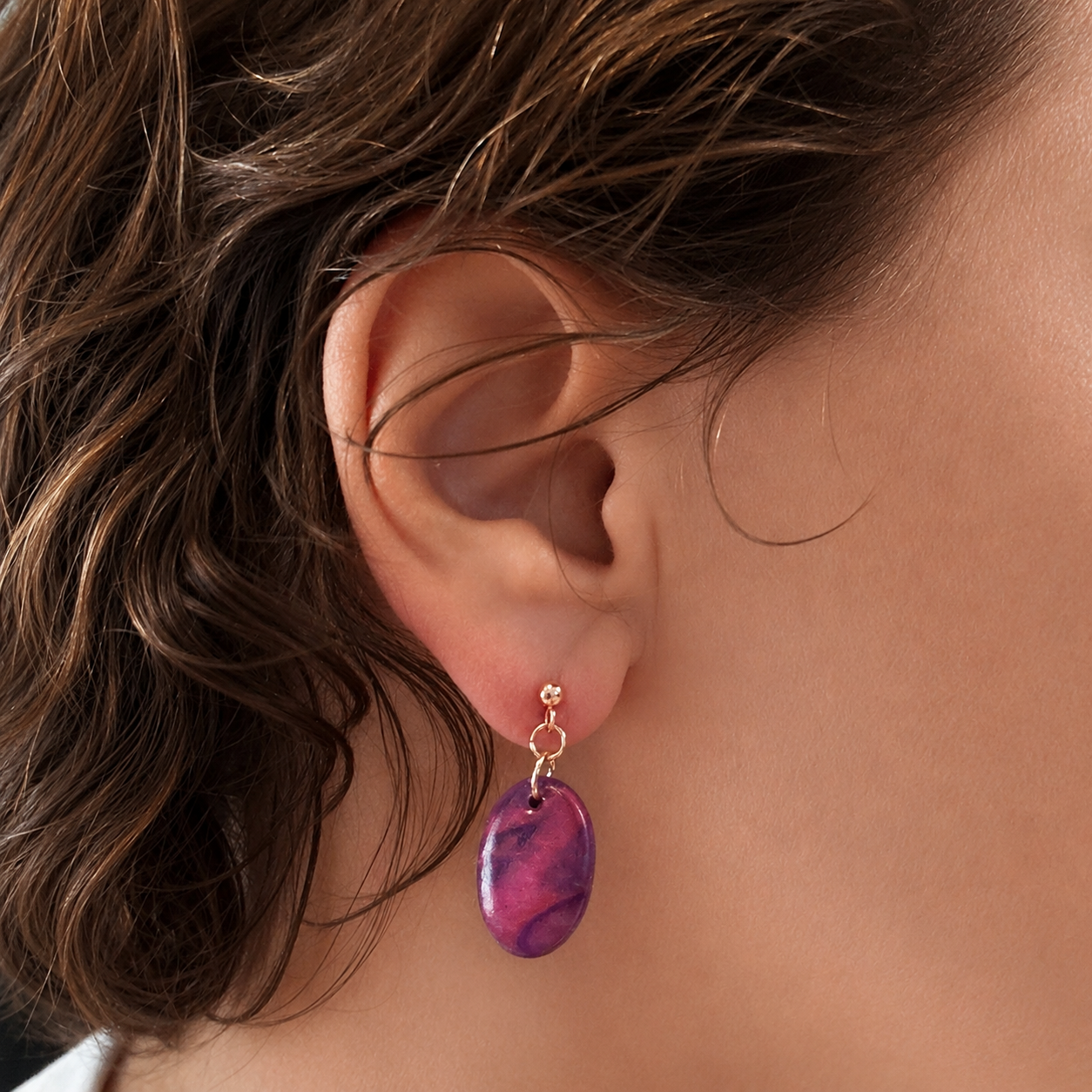 Close of ear wearing purple marbled earring with rose gold findings